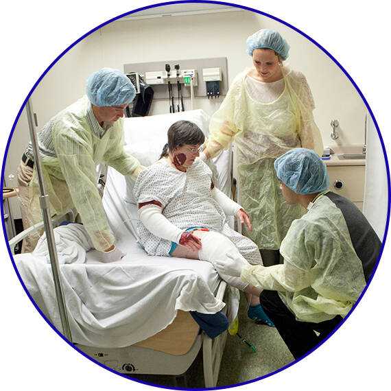 Three students working with a Standardized Patient in a hospital bed during the burn sim.
